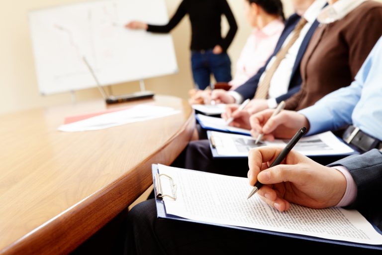 Close-up of businesspeople hands holding pens and papers near table at business seminar