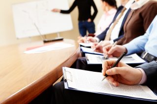 Close-up of businesspeople hands holding pens and papers near table at business seminar